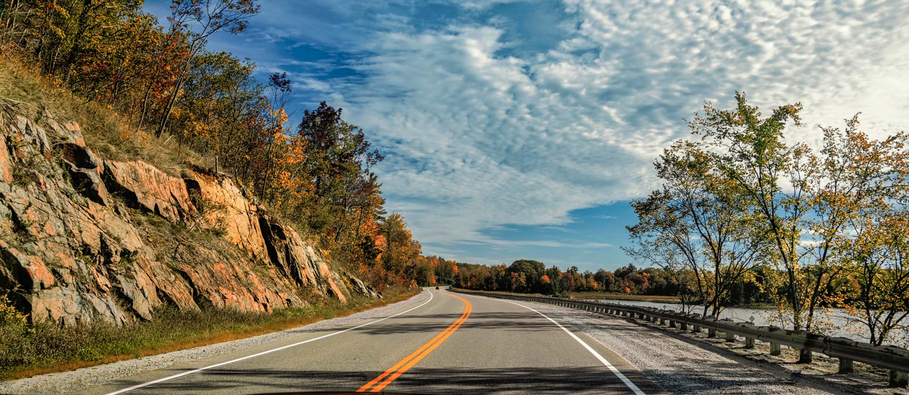 Winding two-lane road along fall coloured mountain and open water