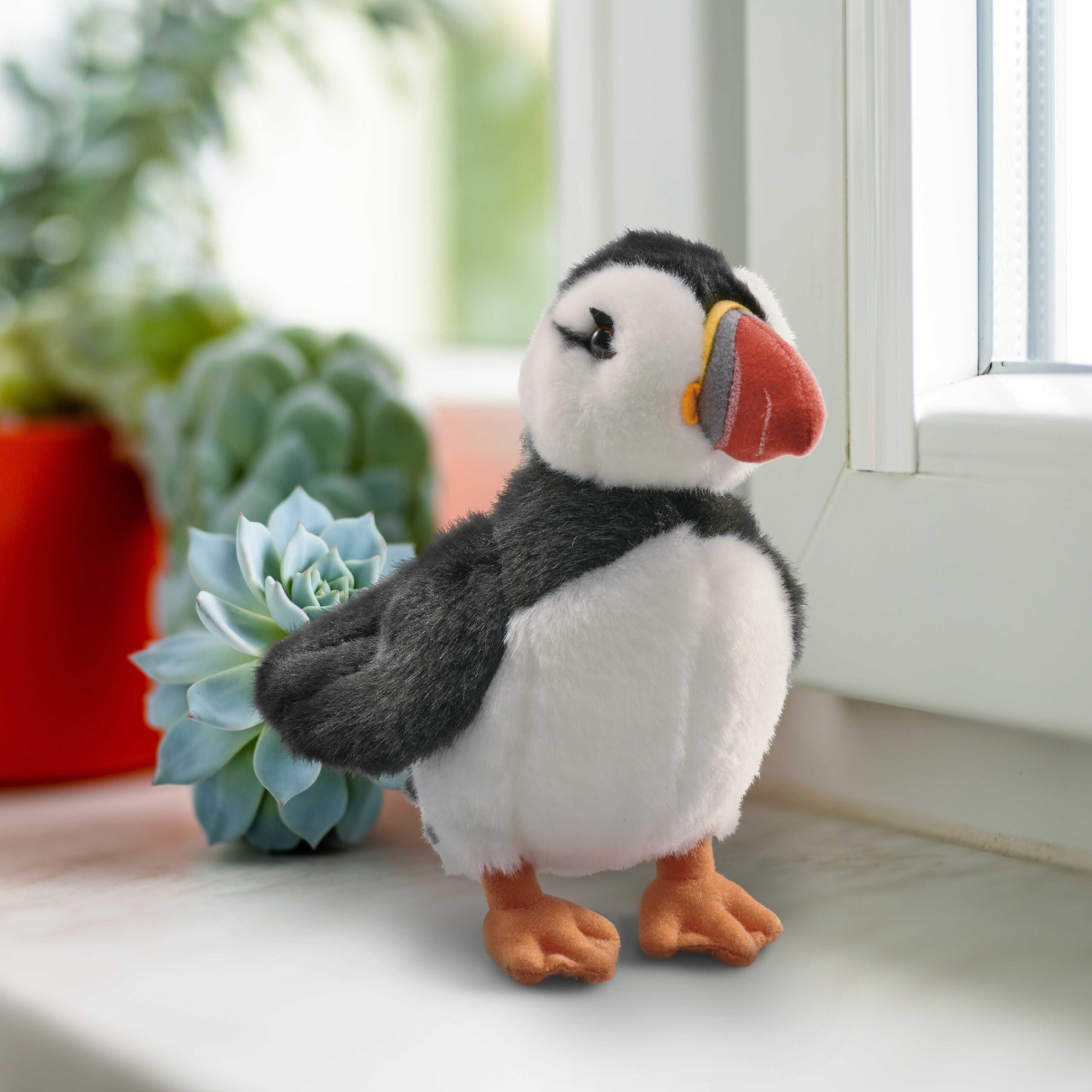 Puffin plush sitting on a windowsill with succulents.