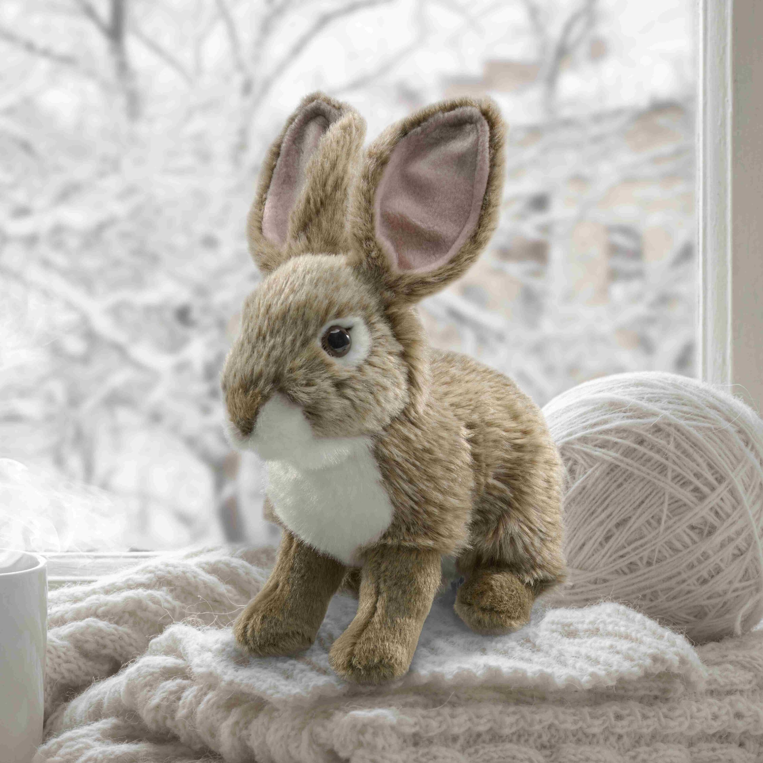 Eastern Cottontail plush sitting on blankets in front of a window showing snowy trees.