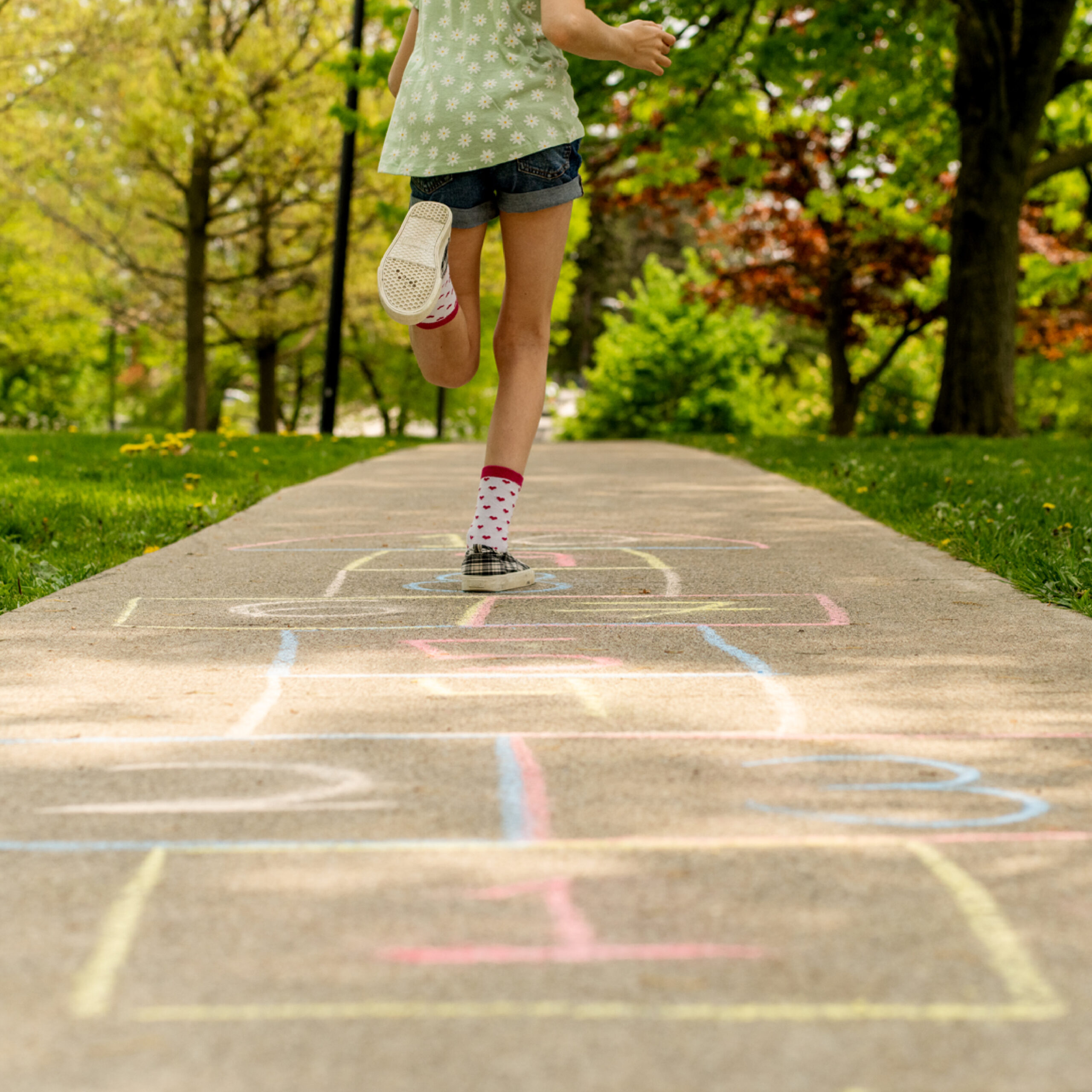 A young child playing hopscotch, jumping away from the camera.