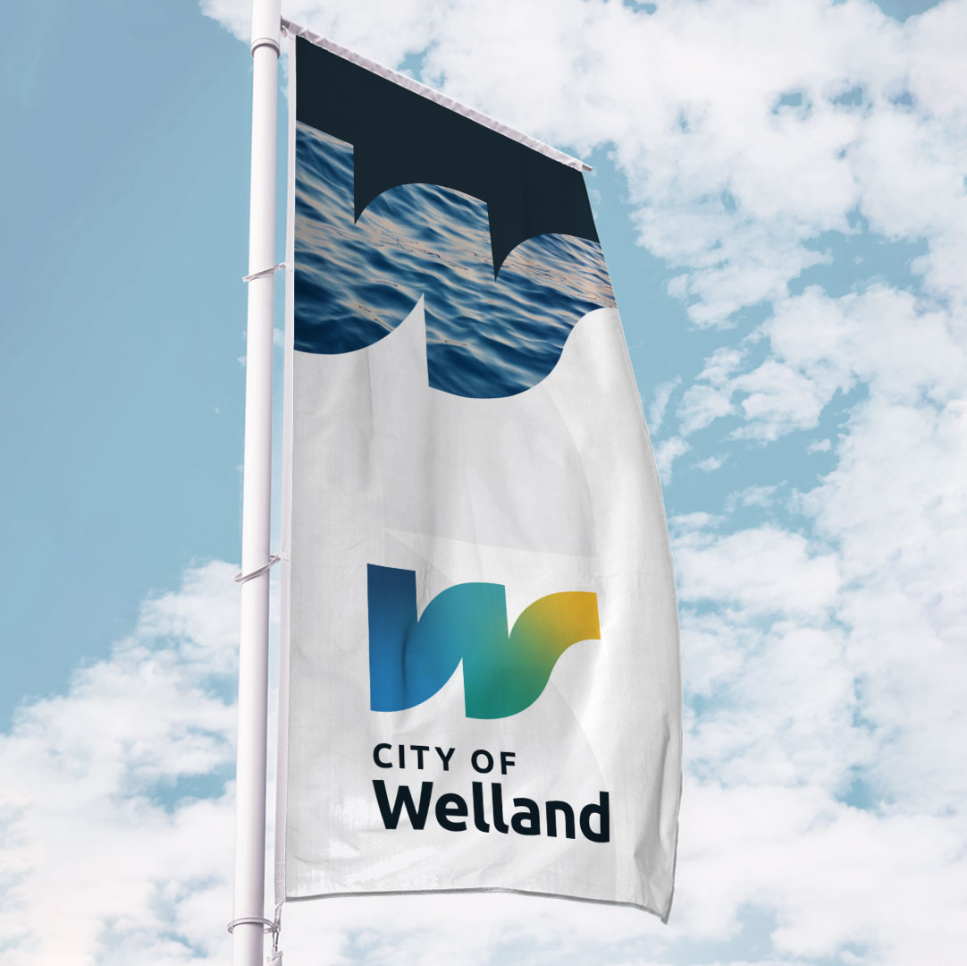 A vertical flag with Welland branding in front of a cloudy blue sky.