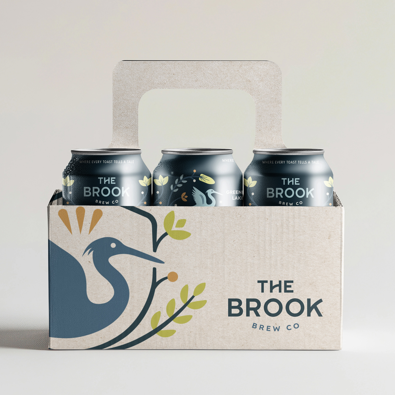 A cardboard six-pack carrier holds three cans of The Brook Brew Co. with a bird and branch illustration on the packaging.