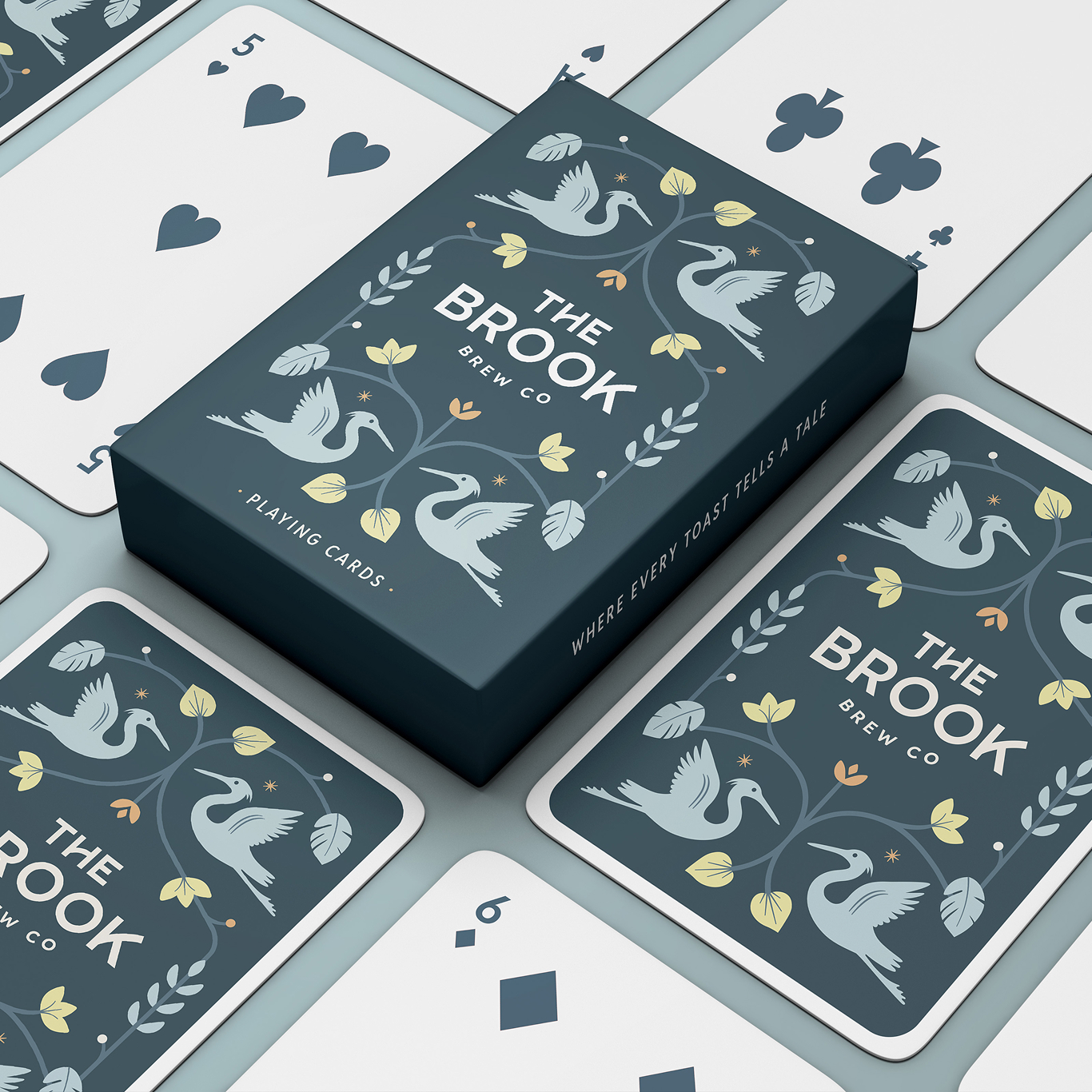A pack of "The Brook Brew Co" playing cards with swan and leaf designs, surrounded by various playing cards.