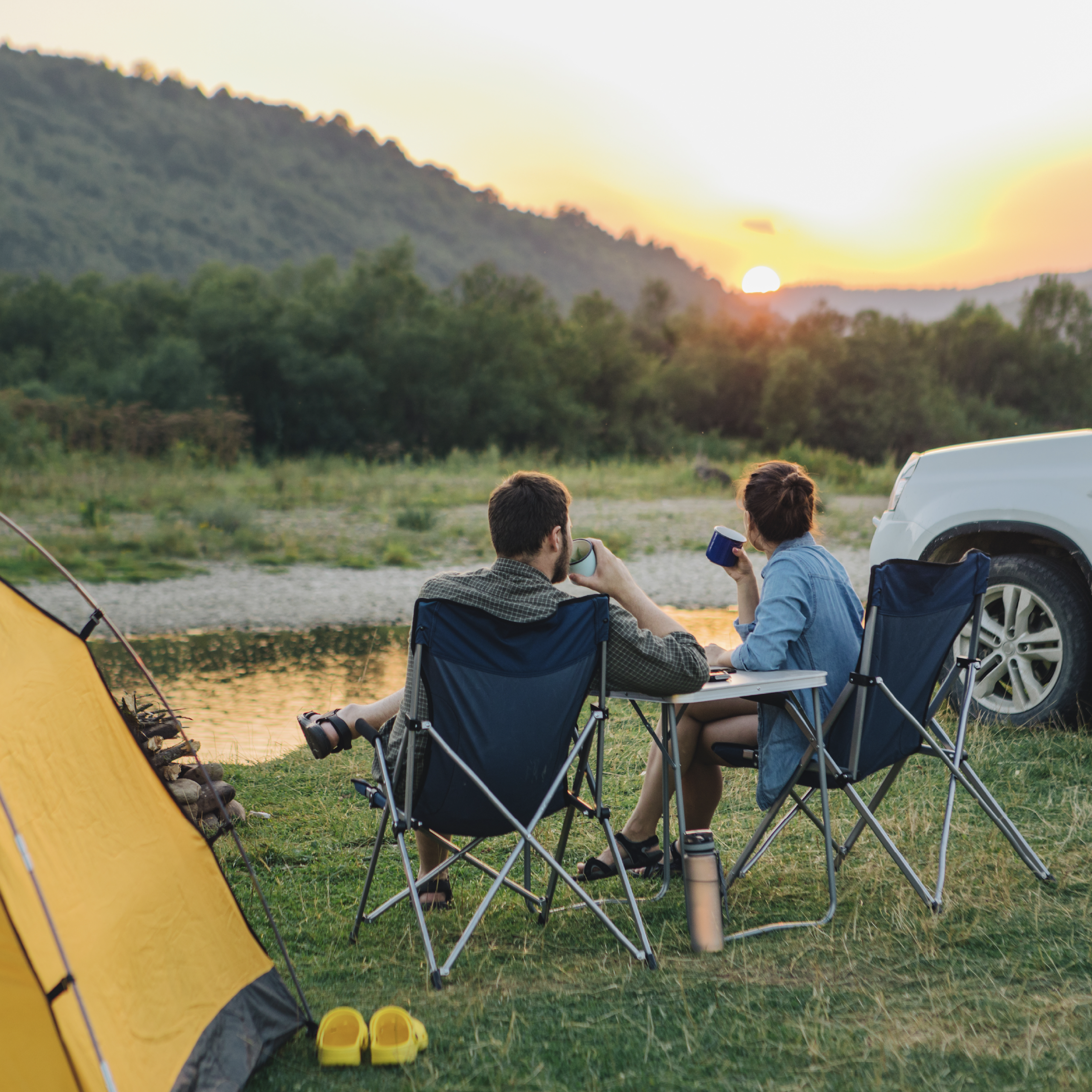 A couple sitting in lounge chairs while enjoying a coffee and watching the sunset camping