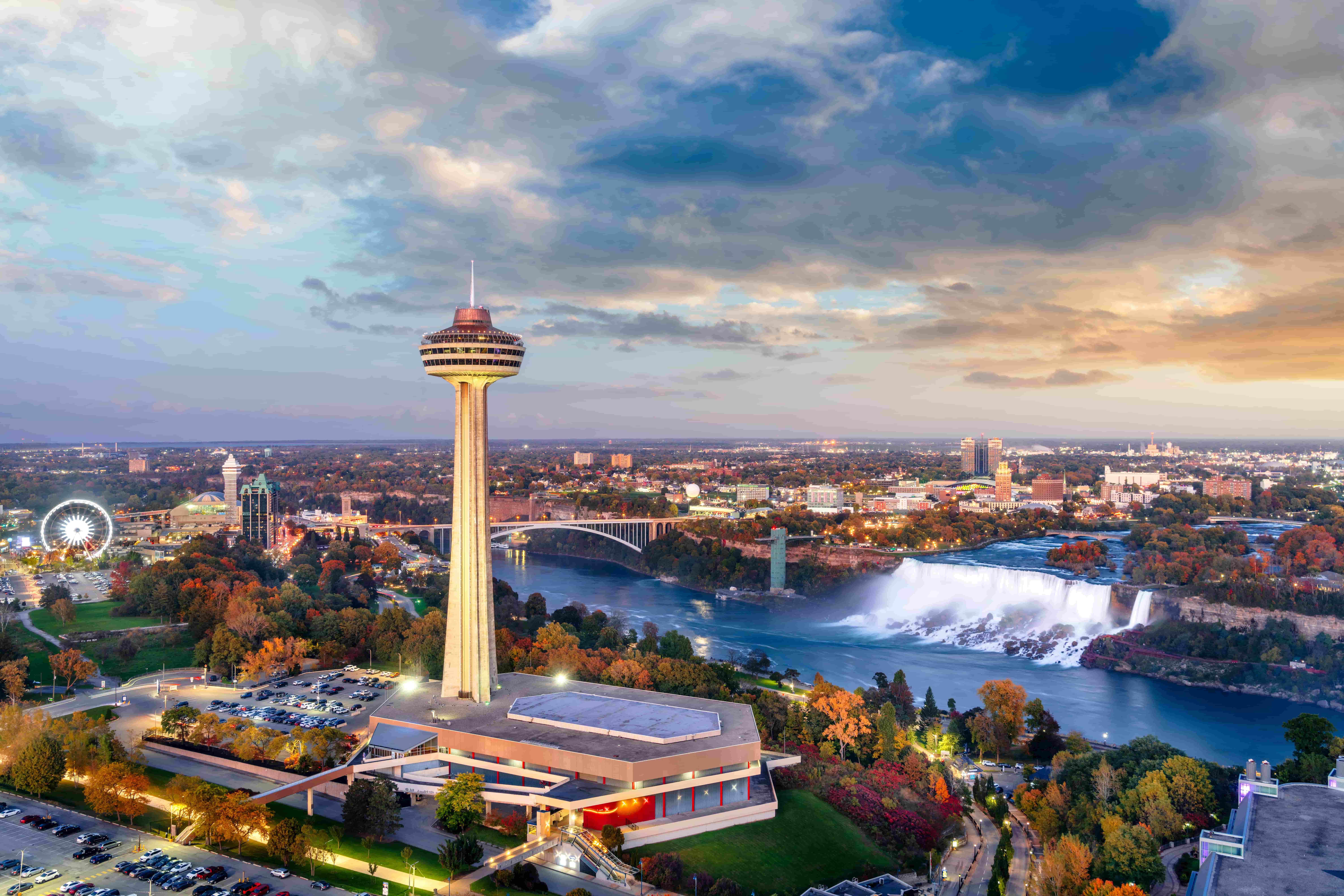 Aerial view of Niagara Falls, the Skylon Tower, and surrounding cityscape at sundown.