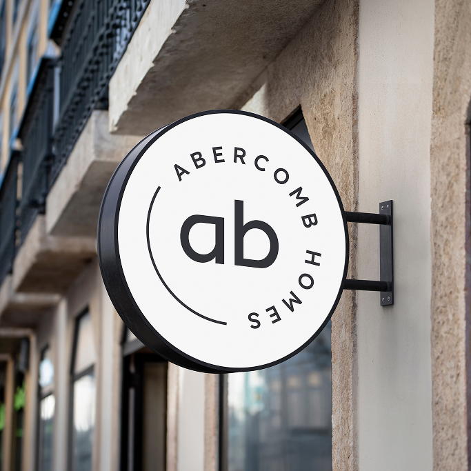 Round wall sign reads "ab" in the centre with "Abercomb Homes" around the edge, mounted on a building exterior.