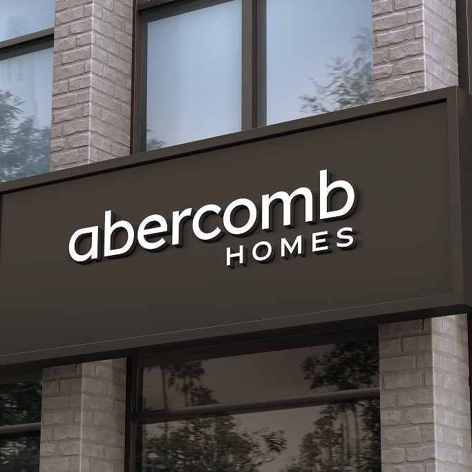 A building facade features a sign reading "abercomb HOMES" in modern white lettering on a dark rectangular background.