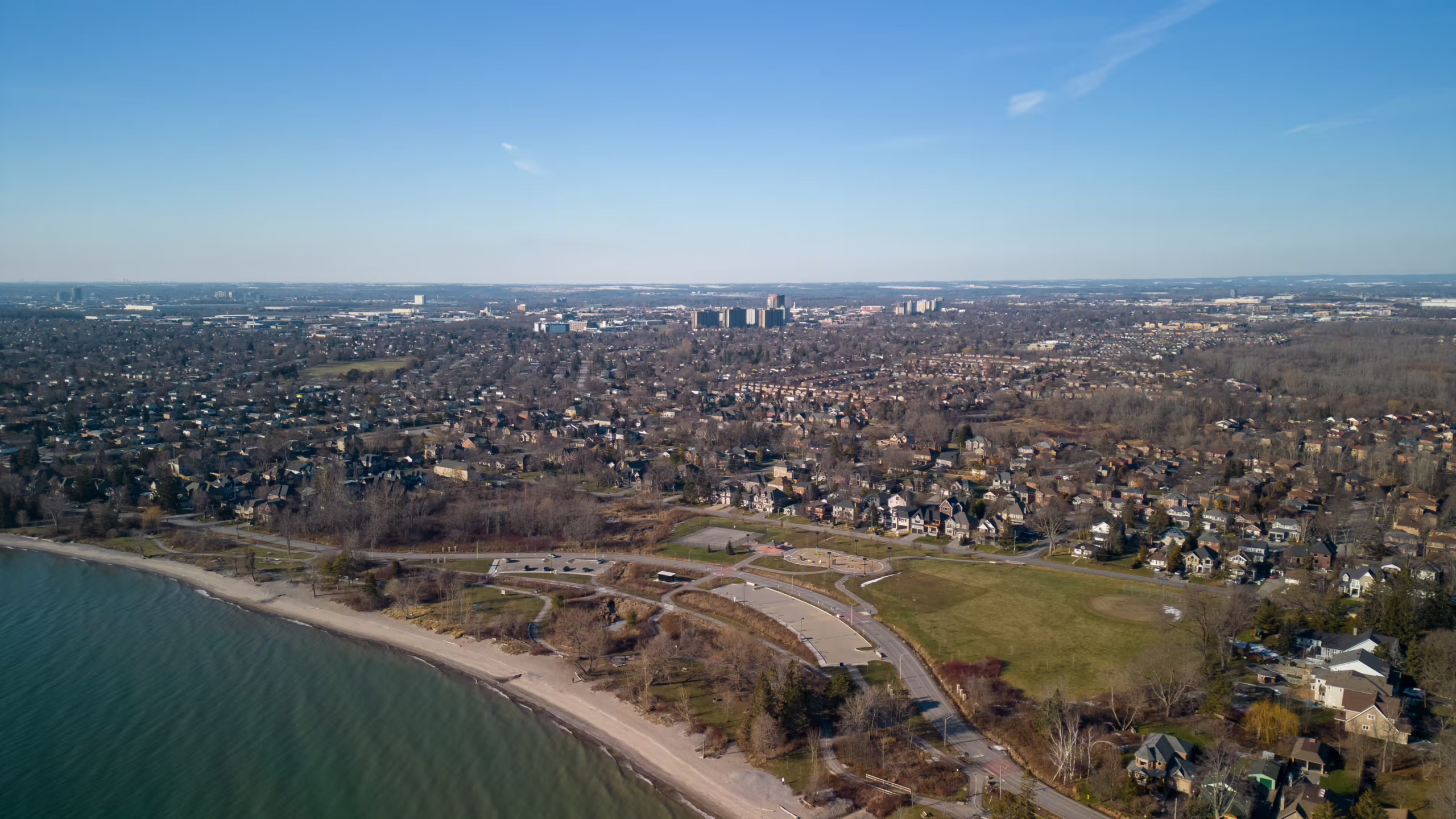 Aerial view of a suburban neighbourhood by a lake, with parks, houses, and city buildings visible in the background.